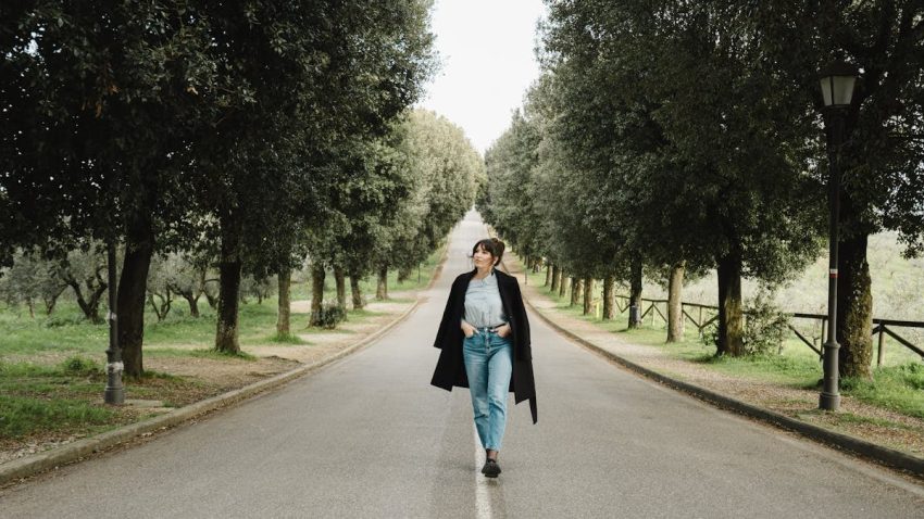 A woman strolls down a picturesque, tree-lined road in Tuscany, capturing a serene yet stylish moment.